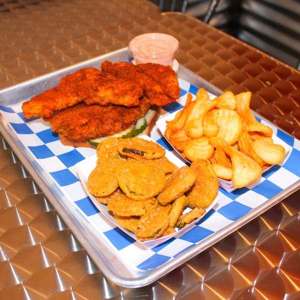 Nashville hot chicken tenders, fried pickles, and crinkle-cut fries on a metal tray with blue checkered paper.