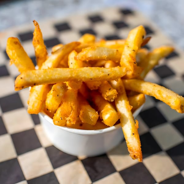A white bowl overflowing with golden, seasoned french fries on a black and white checkered paper.