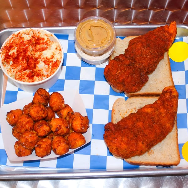 Two Nashville hot chicken tenders on bread, with mac and cheese, tater tots, and sauce.