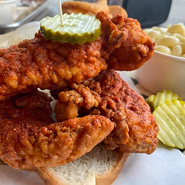 Spicy Nashville hot chicken tenders on white bread, topped with a pickle, with mac and cheese.