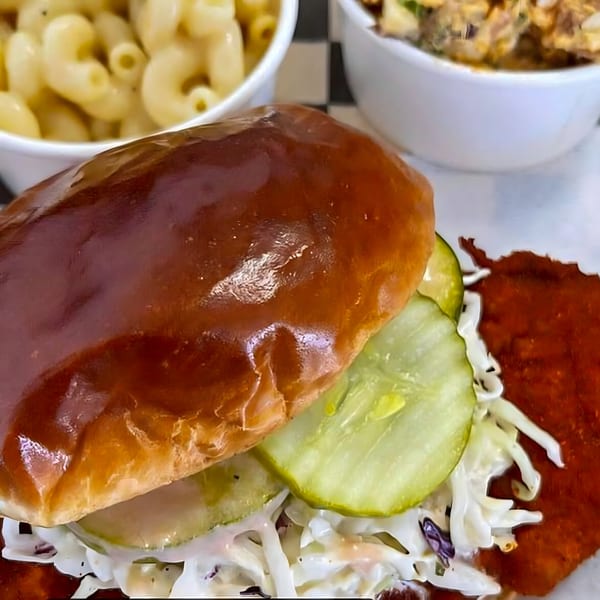 A Nashville Hot Chicken sandwich with pickles and coleslaw, served with mac and cheese.