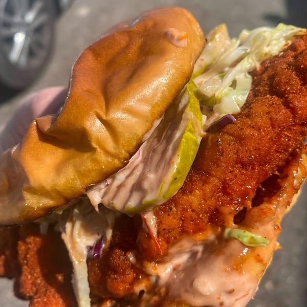 Close-up of a Nashville hot chicken sandwich with pickles, coleslaw, and sauce on a brioche bun.